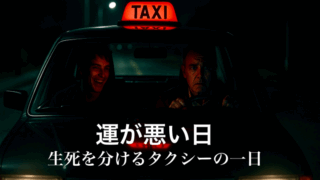 薄暗い夜道を走るタクシーを正面から捉えたシーン。運転席の中年男性は焦りと不安の表情を浮かべ、助手席の若い男は不気味に笑いながら話している。タクシーのヘッドライトが闇を切り裂き、車内には緊迫感が漂っている